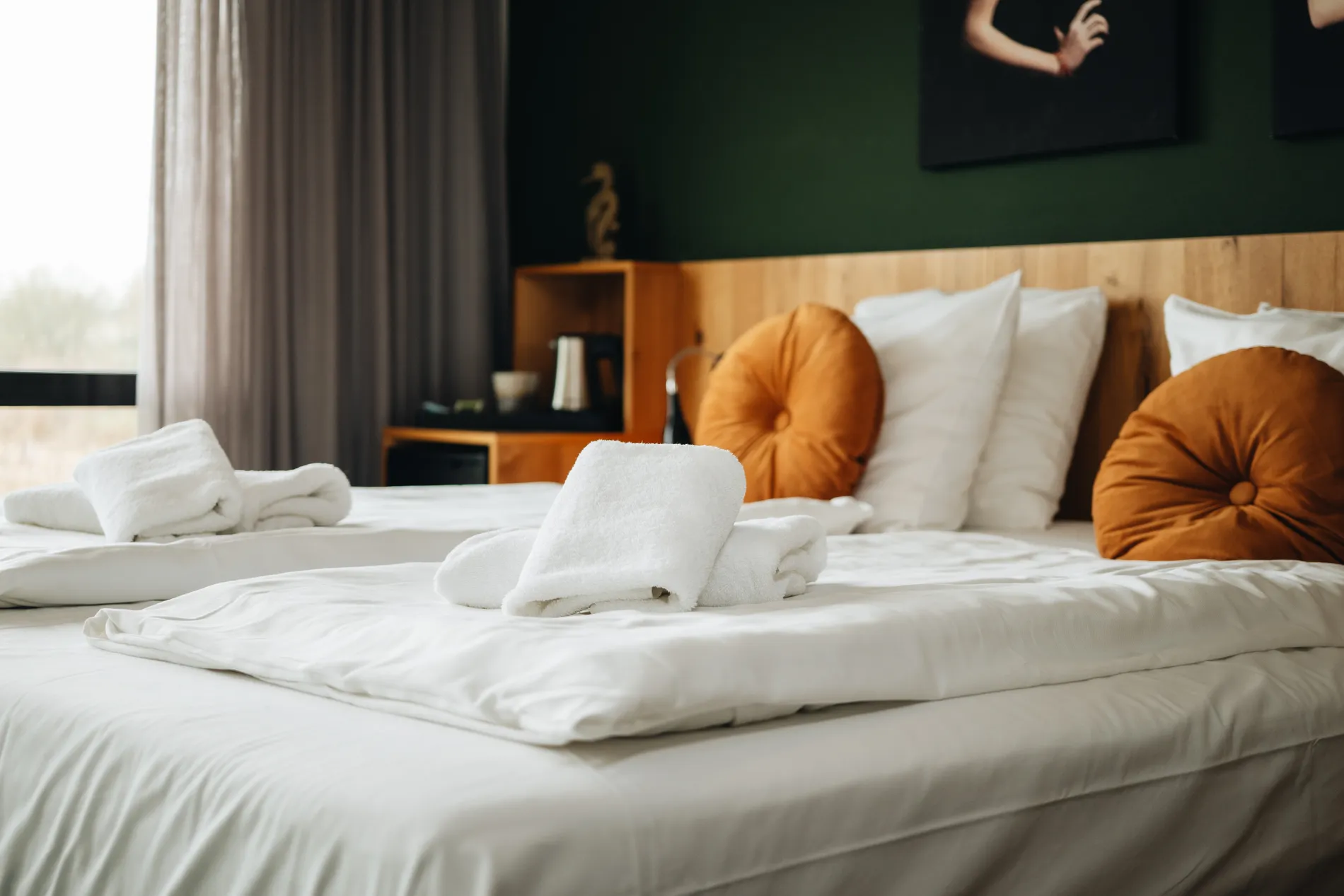 Luxe hotelbed met witte lakens en oranje sierkussens tegen een sfeervolle donkergroene wand met moderne kunst in Resort Land & Zee.